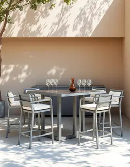 Minimalist outdoor bar set with grey aluminum frame and cream cushioned stools, arranged around a sleek rectangular table holding wine glasses and decanter, set against a soft beige wall with dappled tree shadows, natural daylight, clean lines, modern furniture design, shallow depth of field, 85mm lens, serene patio ambiance, neutral tones, architectural photography.